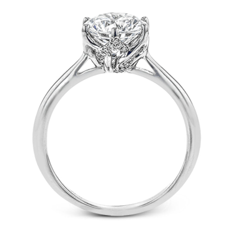 This 18k white gold engagement ring looks deceptively simple at first, but reveals its intricacy upon closer inspection. Accents of .05 ctw of diamonds decorate the sides of the six-prong center stone setting, creating a stunning effect.