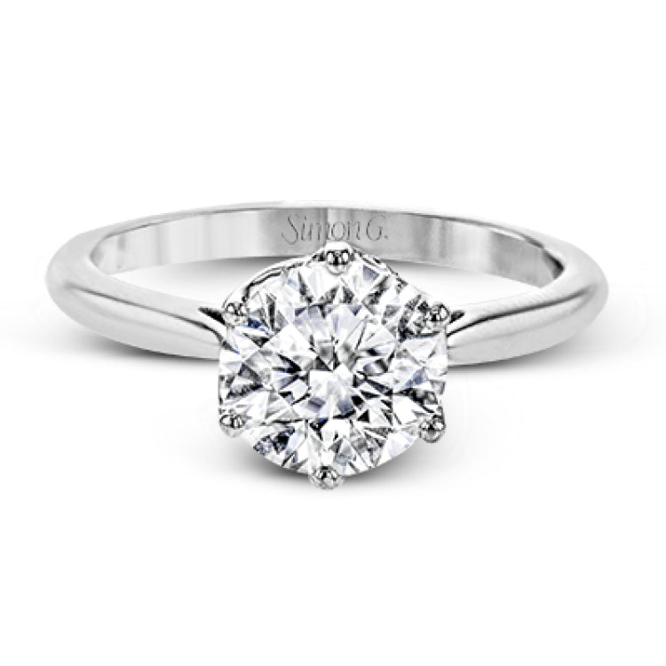 This 18k white gold engagement ring looks deceptively simple at first, but reveals its intricacy upon closer inspection. Accents of .05 ctw of diamonds decorate the sides of the six-prong center stone setting, creating a stunning effect.