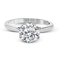 This 18k white gold engagement ring looks deceptively simple at first, but reveals its intricacy upon closer inspection. Accents of .05 ctw of diamonds decorate the sides of the six-prong center stone setting, creating a stunning effect.