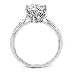 This 18k white gold engagement ring looks deceptively simple at first, but reveals its intricacy upon closer inspection. Accents of .05 ctw of diamonds decorate the sides of the six-prong center stone setting, creating a stunning effect.