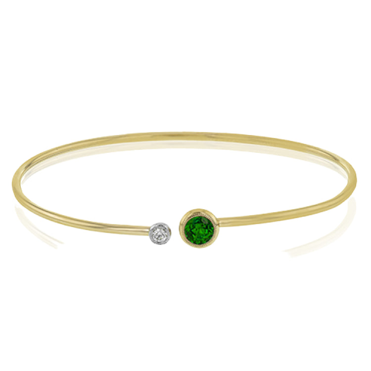 This understated yellow gold bangle features a subtle .08 ctw white diamond accent opposite a stunning .65 ctw emerald. Perfect for stacking.