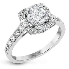 This sleek, contemporary white gold engagement ring contains .35 ctw of round white diamonds and .19 ctw of baguette shaped diamonds on its shank and unique, geometric halo