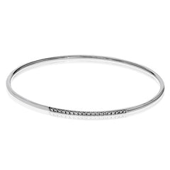 This lovely 18k white gold bangle contains .13 ctw of white diamonds in a simple line. This bangle is perfect for stacking, or making a delicate statement all on its own.