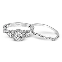 This 18k white gold wedding set has a distinctive design with a milgrain accented bezel center stone setting, .15 ctw pear side stones, and .50 ctw of round brilliant diamonds.