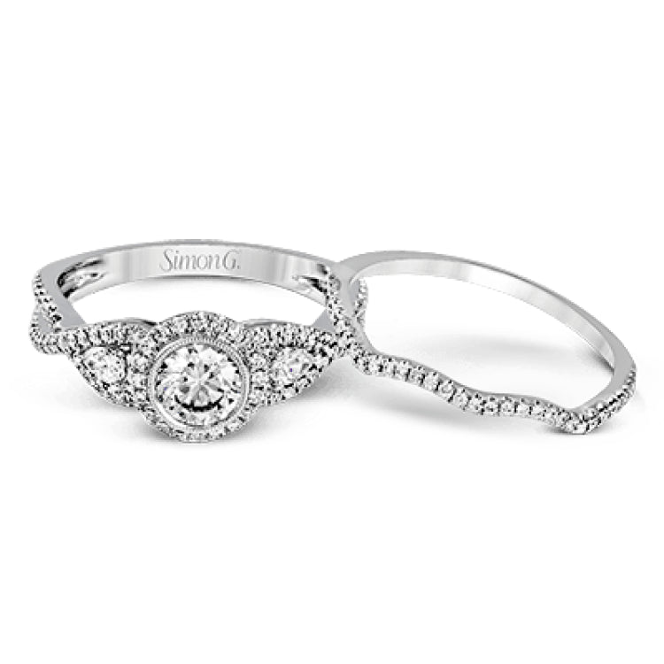 This 18k white gold wedding set has a distinctive design with a milgrain accented bezel center stone setting, .15 ctw pear side stones, and .50 ctw of round brilliant diamonds.